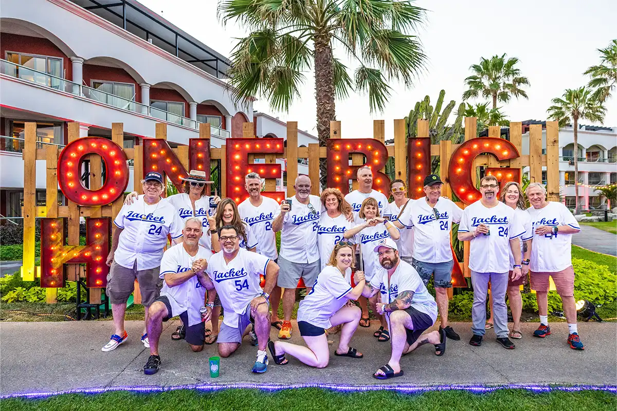 A group photo in front of a One Big Holiday light up sign, matching baseball jersey themed outfits.