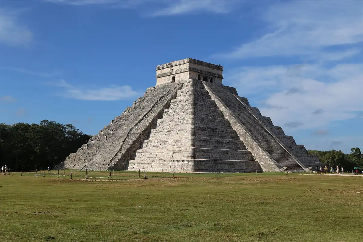 A mayan temple in the middle of a grass field.