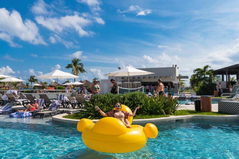 A guest sitting on a giant pool inflatable with their hands up.